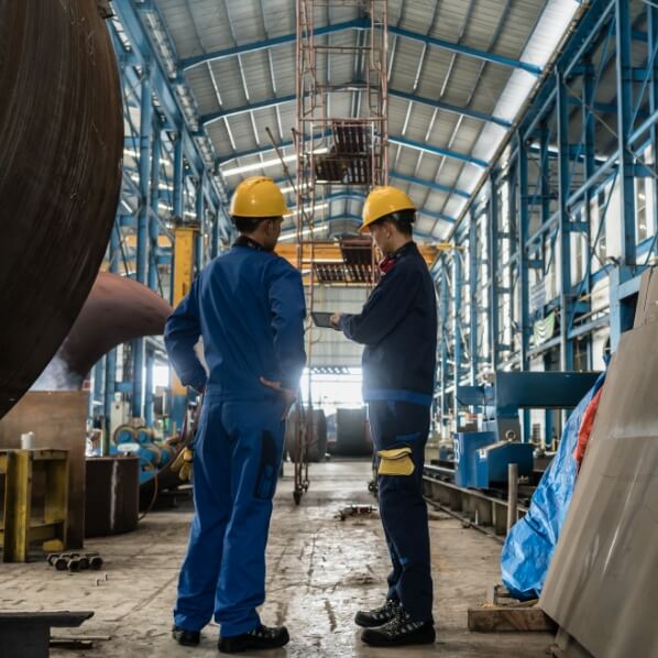 Two male workers in PPE having a discussion in a steel plant.