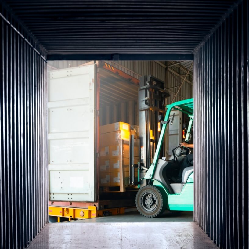 Forklift driver loading a shipping container.