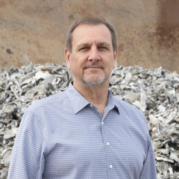 CEO, Mike Uhrick, headshot, against steel plate and pile of shredded aluminum scrap metal.